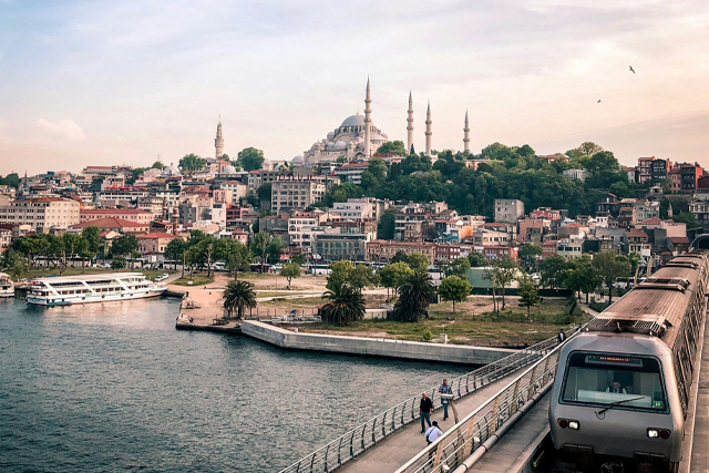 A scenic view of Istanbul featuring the metro crossing the Golden Horn, with Suleymaniye Mosque and the historic cityscape in the background.