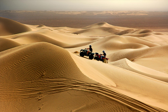 Two riders on quad bikes exploring the golden sand dunes of the desert.