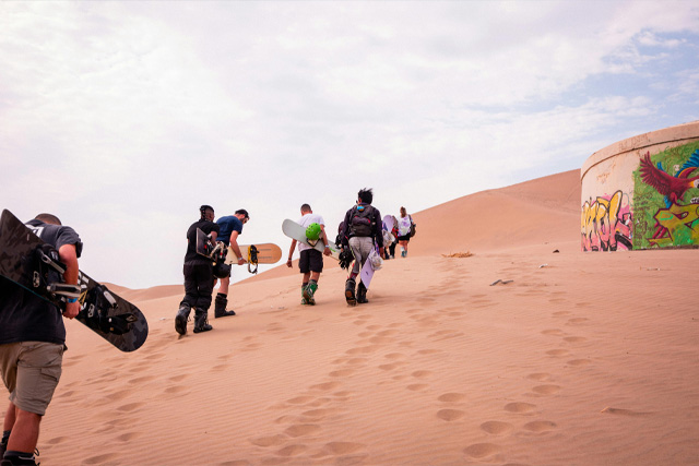 A group of young adventurers sandboarding down the golden dunes in the desert