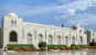 A stunning white marble building with intricate Islamic architecture, arched windows, and lush gardens in Oman.