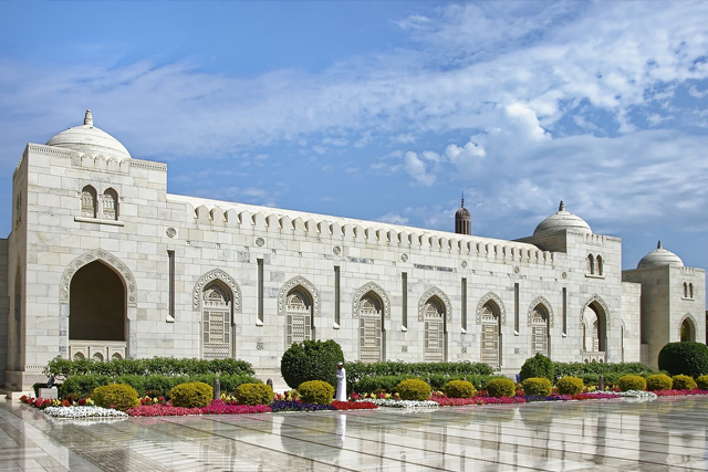 A stunning white marble building with intricate Islamic architecture, arched windows, and lush gardens in Oman.