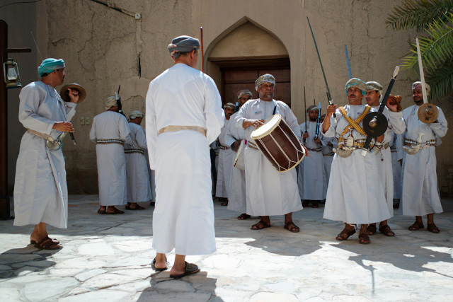 Traditional Omani performance in Nizwa, featuring men dressed in white dishdashas playing drums and swords in a cultural ceremony.