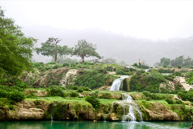 A breathtaking waterfall cascading into a turquoise pool, surrounded by lush greenery in Salalah, Oman.